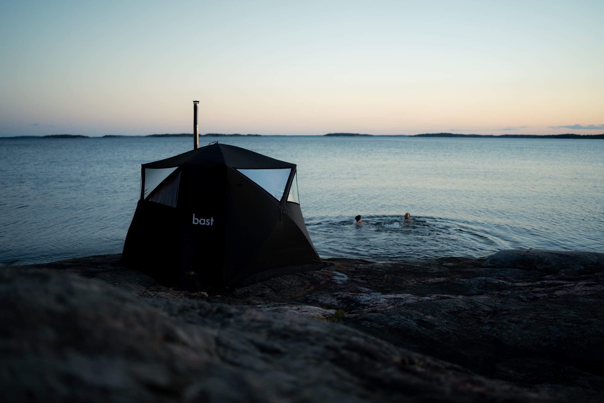 Bast Näver sauna tent on a Swedish archipelago rock at sunset, with two bathers in the sea nearby