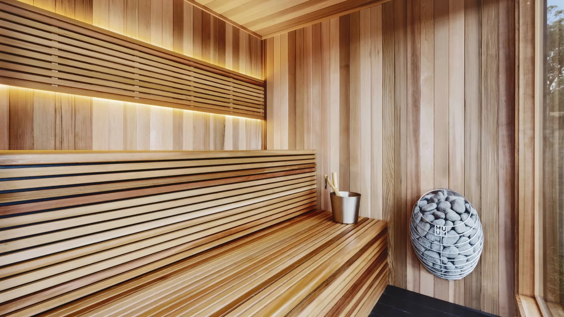 HUUM DROP electric heater with stone-clad body in a modern cedar sauna with bench-edge LED lighting
