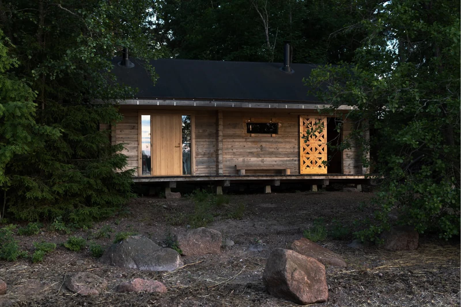 Narvi wood-burning sauna cabin glowing warm through a lattice door at dusk in a Finnish forest