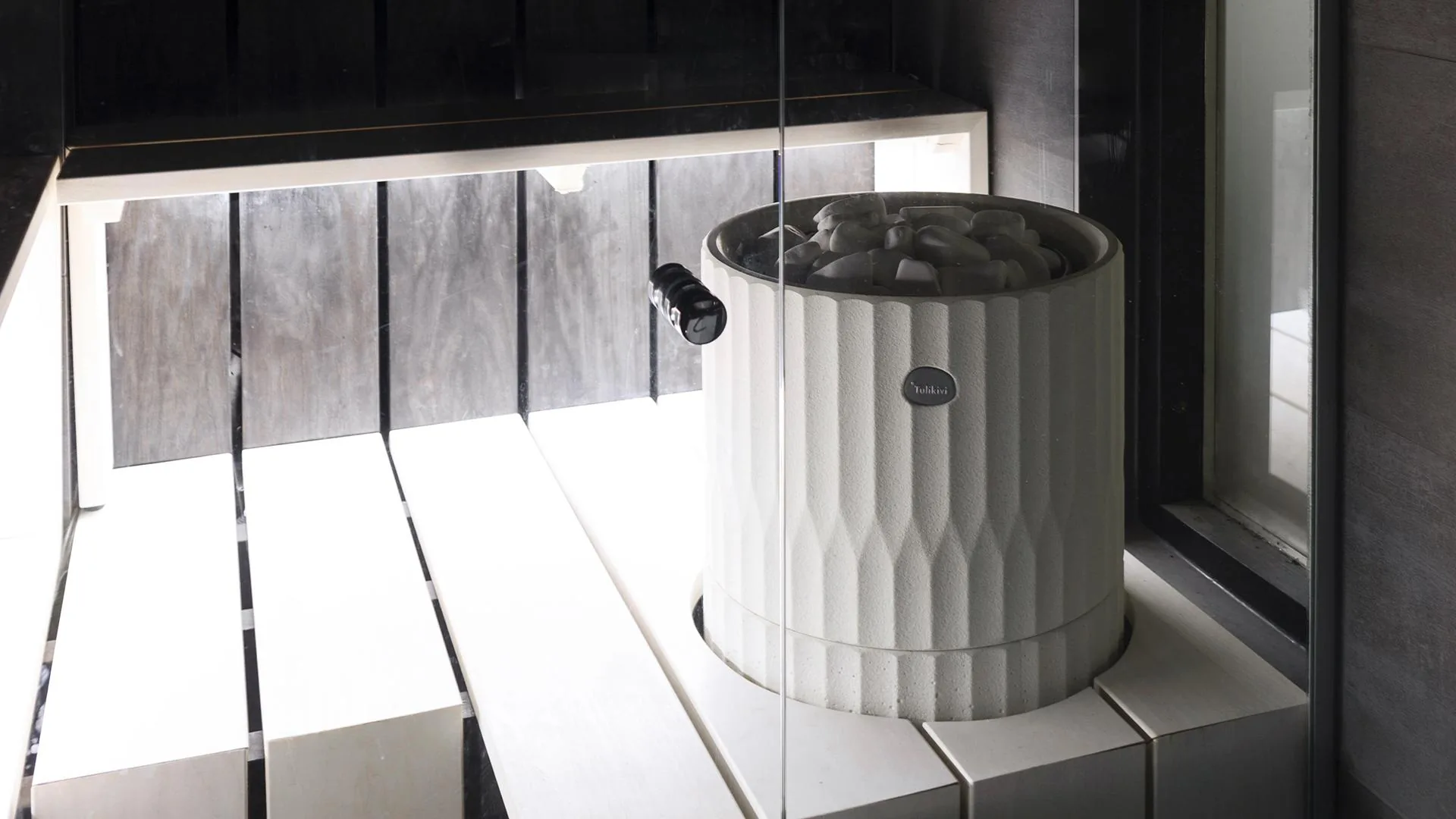 Tulikivi Riite white electric heater in a dark-walled sauna with slatted window