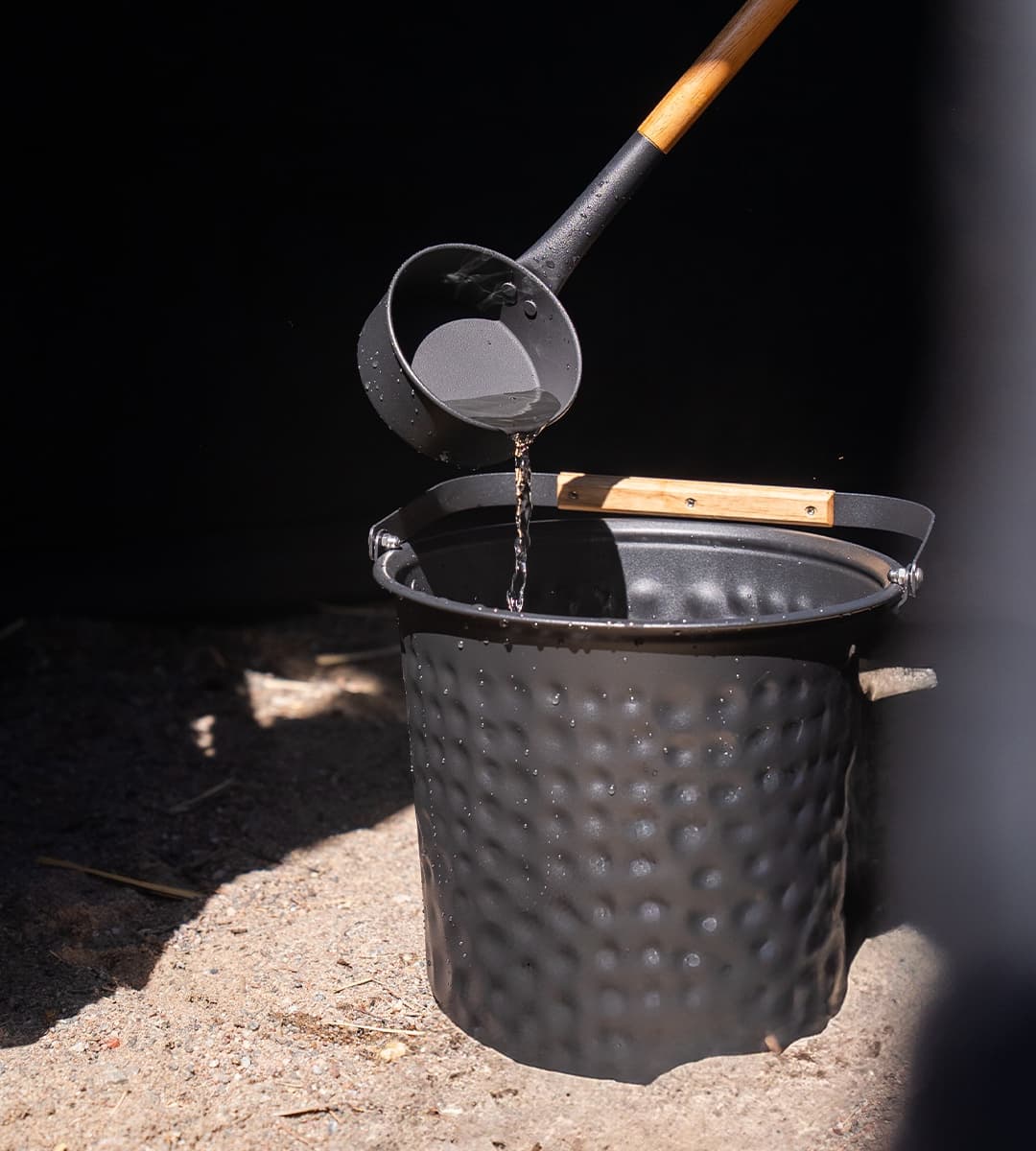 Bast hammered-black sauna bucket and wooden-handled ladle with water droplets