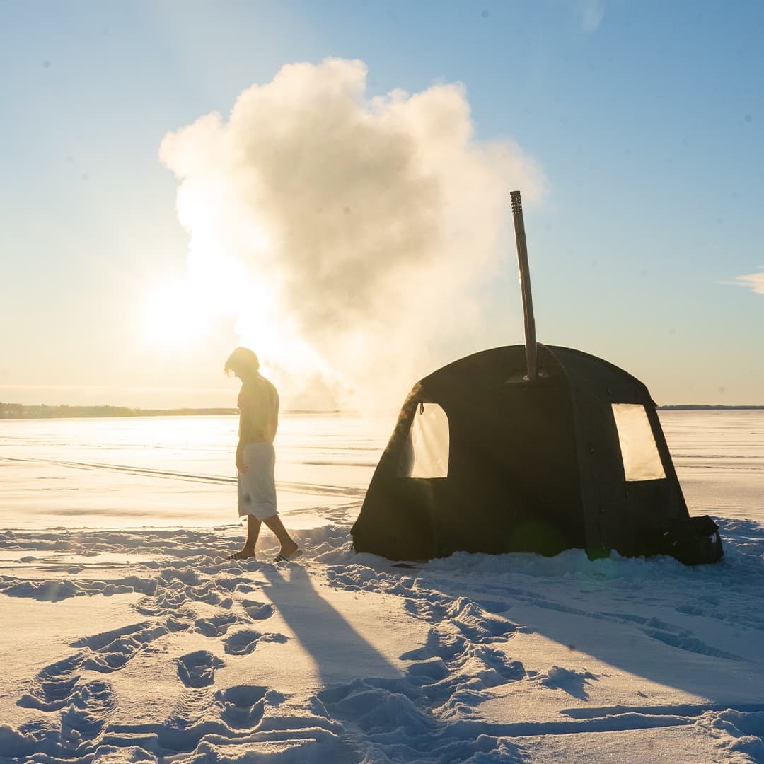 Silhouette of a bather beside the Näver at golden hour with steam rising from the stove chimney
