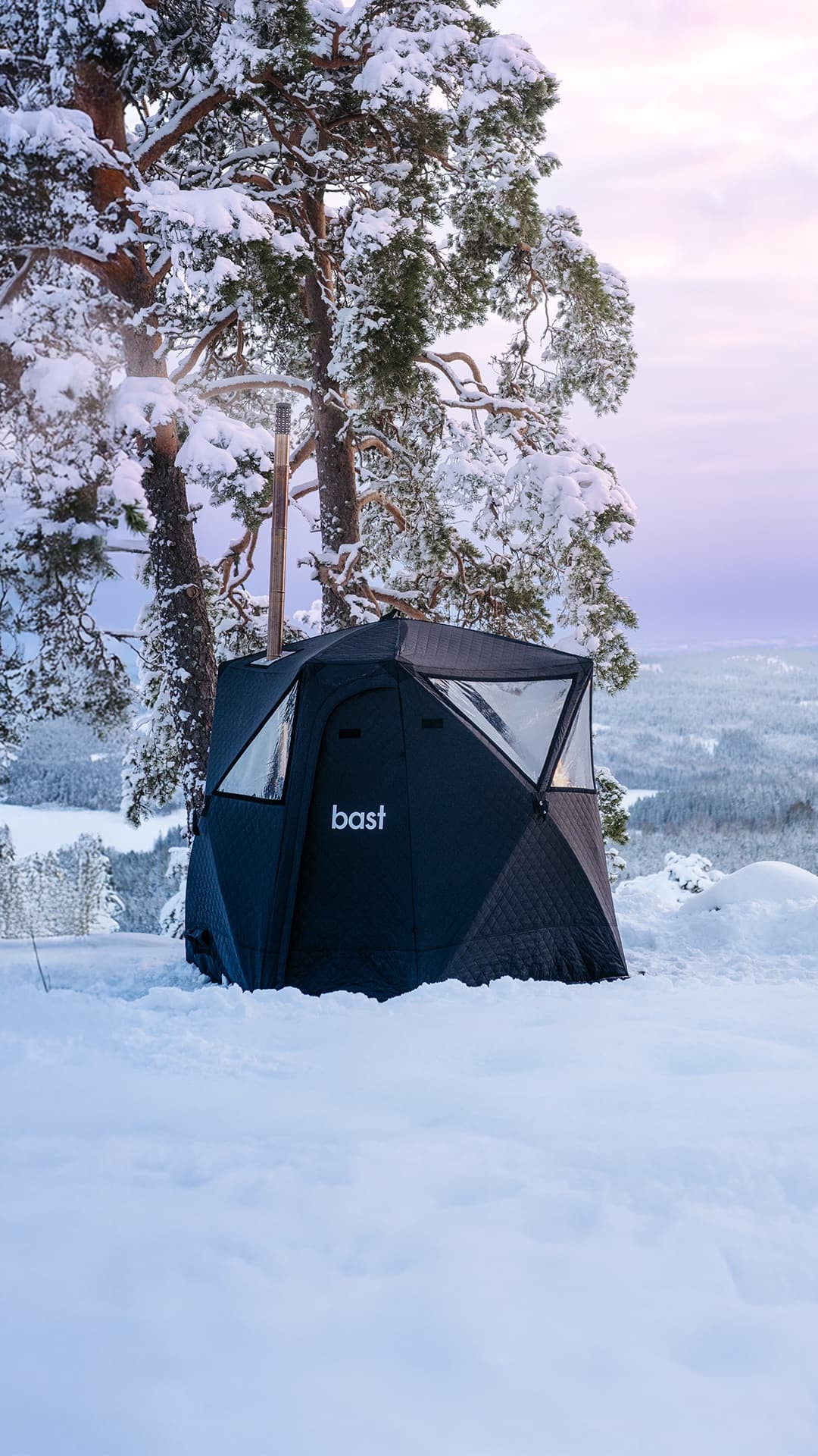 The Näver sauna tent nestled in snow with pine trees and a pink arctic sky at dusk