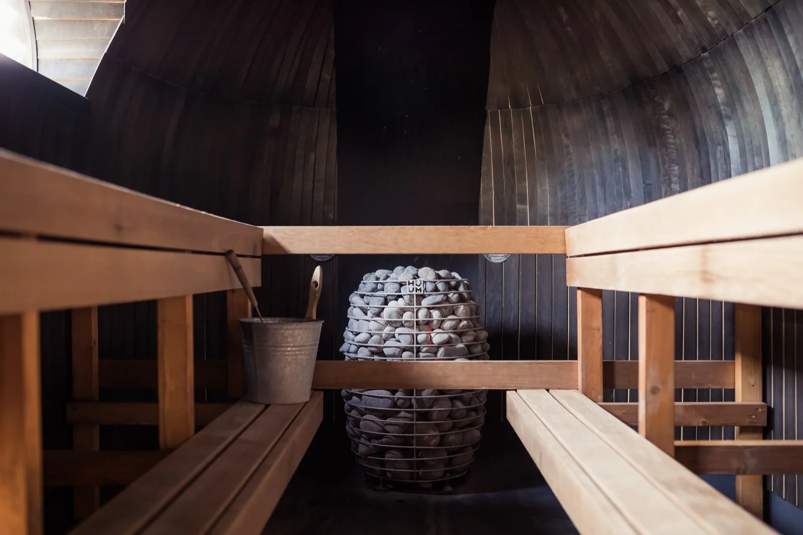 HUUM HIVE stone heater inside a black barrel sauna with cedar benches