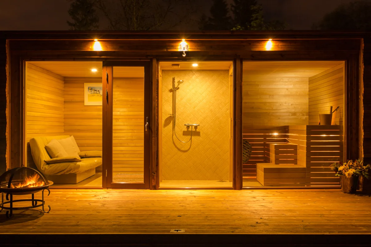 HUUM outdoor sauna cabin lit from inside at night, fire pit on the deck